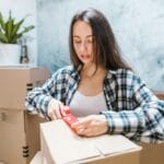 Kobieta zakleja kartony taśmą podczas pakowania do przeprowadzki