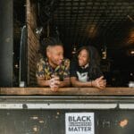 Uśmiechnięci przedsiębiorcy przy oknie z transparentem Black Businesses Matter