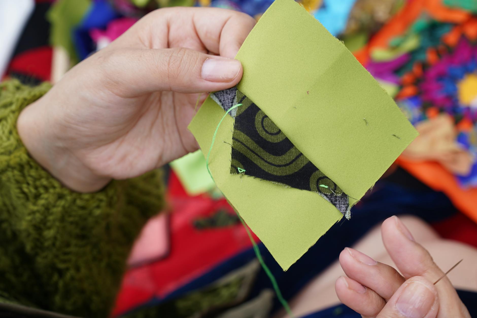 Dłonie szyjące kolorową narzutę patchworkową z różnych tkanin